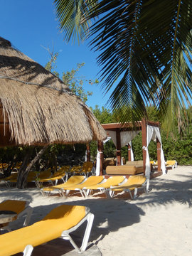 Outdoor lounge bed, straw umbrella and folding chairs on a Caribbean beach in Riviera Maya, Mexico, for travel backgrounds