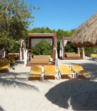 Outdoor lounge bed, straw umbrella and folding chairs on a Caribbean beach in Riviera Maya, Mexico, for travel backgrounds