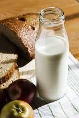 Glass bottle with milk, black bread and apples on a wooden table. Country still life with farm products.