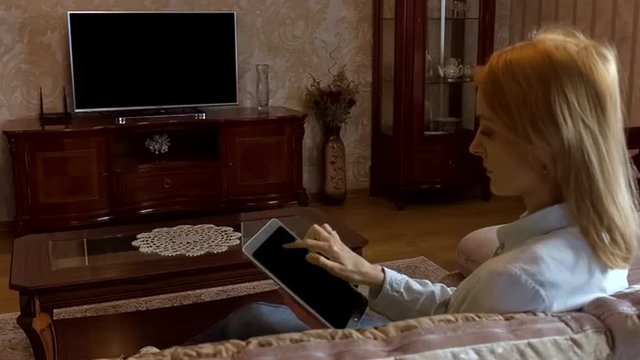 Young woman using tablet and watching television in living room. Shoot behind model's shoulders. Alpha Channel included.