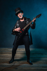 Heavy metal senior man with electric guitar in front of dark blu