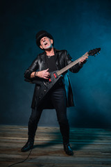 Fototapeta premium Heavy metal senior man with electric guitar in front of dark blu