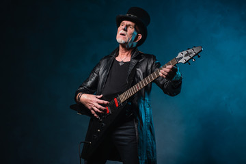 Fototapeta na wymiar Heavy metal senior man with electric guitar in front of dark blu