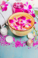 Yellow bowl with water and pink orchid flowers , white towel , lotion bottle  and cream jars on mint blue wooden background. Spa, wellness or body care concept