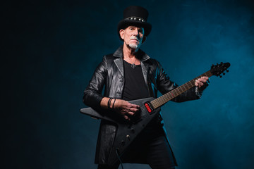 Heavy metal senior man with electric guitar in front of dark blu