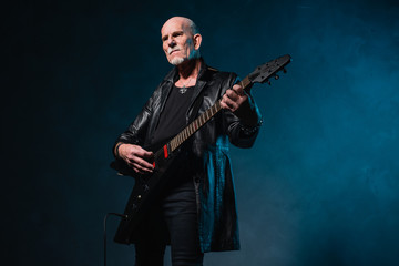 Fototapeta premium Bald heavy metal senior man with electric guitar in front of dar