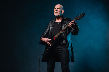Bald heavy metal senior man with electric guitar in front of dar