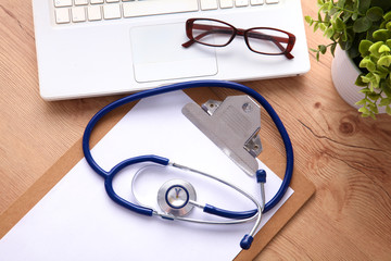 A medical stethoscope near a laptop on a wooden table, on white