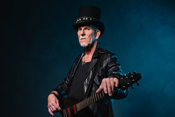Heavy metal senior man with electric guitar in front of dark blu