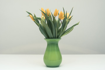 Bouquet of yellow tulips in a green vase standing on a white table