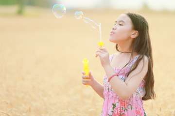 child girl blowing soap bubbles at sunset