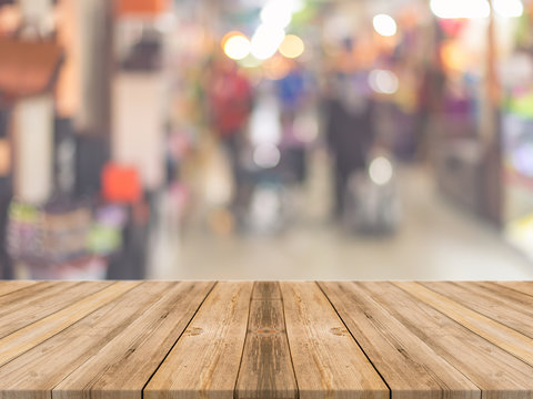 Wooden board empty table in front of people shopping at market fair background. Perspective wood and blur market - can be used for display or montage your products - vintage effect style pictures.