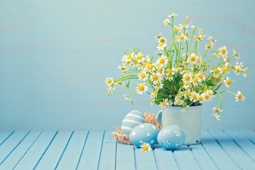 Easter holiday decoration with daisy flowers and painted eggs on wooden blue table