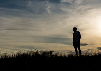 Man in silhouette standing on hill contemplating life and enjoying the view