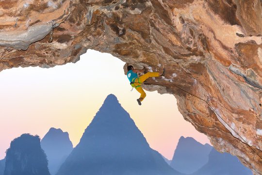 Rock Climber assaulting overhanging rocky Roof karst Mountains Background