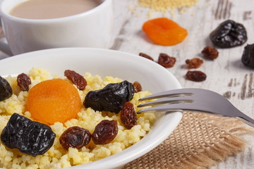 Cooked millet groats on white plate and cup of coffee with milk, healthy food and nutrition