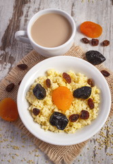 Cooked millet groats on white plate and cup of coffee with milk, healthy food and nutrition