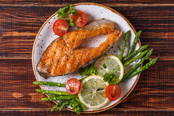 Grilled salmon steak served with asparagus, tomato and lemon.
