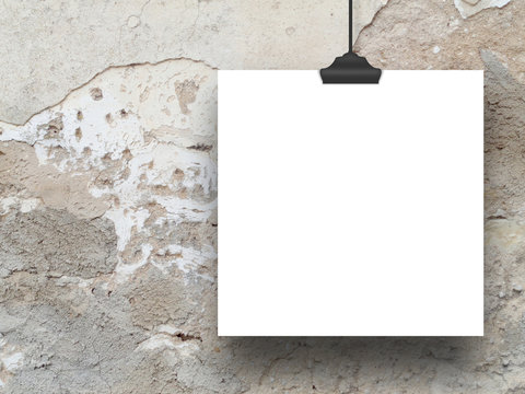 Close-up of one square paper sheet with clip on scratched and cracked plaster wall background