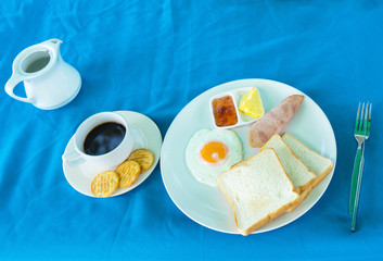 Fried egg, toast, cup of coffee, butter and jam on the table, top view.