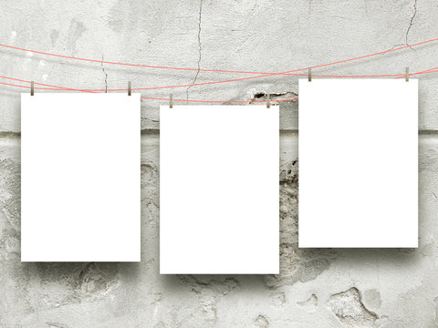 Close-up of three hanged paper sheets with pegs on cracked concrete wall background