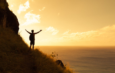Happy man on top a mountain reaching his army out toward the horizon. Healthy lifestyle and life achievement concept. 
