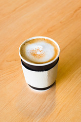 A paper cup containing a hot coffee on wooden table