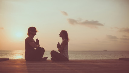 Young couple is doing yoga on the sunrise background.