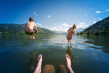 girl and boy jumping in lake water at summer holiday