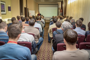 The audience listens to the acting in a conference hall. Pass through the center of the room between the rows toward the screen.