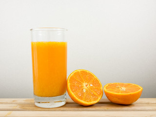 The glass of tasty pure orange juice and fresh orange half on wooden tray for a good healthy.