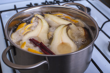 Pears on sugar syrup with lemon slices and cinnamon stick, pot of syrup on the stove.