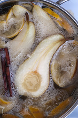 Pears on sugar syrup with lemon slices and cinnamon stick, pot of syrup on the stove.