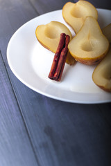 Pears cooked in sugar syrup with cinnamon stick on white plate on blue wooden table. 
Selective focus.