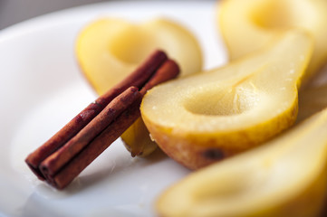 Closeup of Pears cooked in sugar syrup with cinnamon stick on white plate