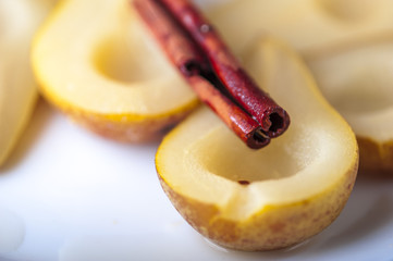 Closeup of Pears cooked in sugar syrup with cinnamon stick on white plate