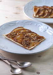 Tarte with puff pastry, pears, walnuts on white plate, silver spoons on wooden table