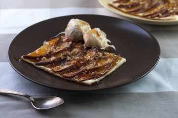 Tarte with puff pastry, pears, walnuts and ice cream on brown plate and silver spoon