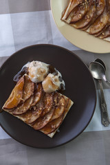 Tarte with puff pastry, pears, walnuts and ice cream on brown plate and silver spoons