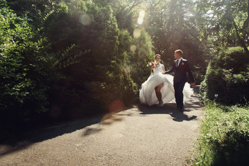 Romantic beautiful newlywed couple walking & posing in sunlit pa