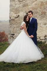 Happy newlywed couple hugging near old castle wall