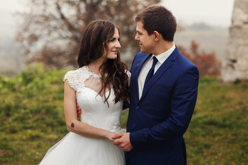Happy newlywed couple hugging near old castle wall
