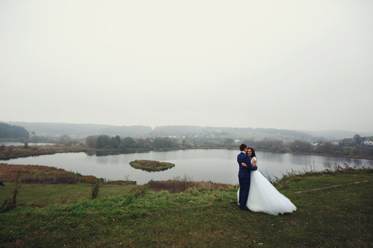 Happy beautiful couple of newlyweds hugging near romantic lake