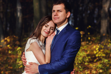 Romantic, happy newlywed couple hugging in autumn park at sunset