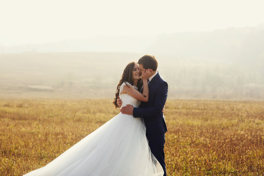 Romantic fairytale newlywed couple hug & smile in field at sunse