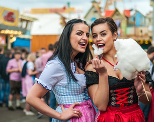 Two young women in Dirndl dress or tracht, laughing with cotton candy floss at the Oktoberfest