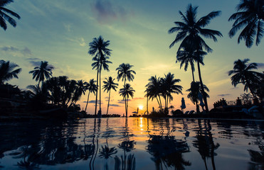 Beautiful sunset on a tropical beach with palm trees reflection in the water.