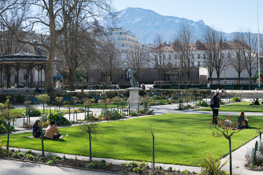 Square, herbe et gens assis dans le Jardin de ville &agrave; Grenoble, lors d'un dimanche d'hiver ensoleill&eacute;, plan large