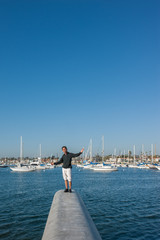 Middle age man balances on concrete ledge over marina.