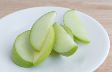 Close view of green apple slices on a white plate atop a wood table top